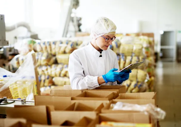 Medewerkster in hygiënekledij controleert dozen aan een voedingsverpakkingslijn