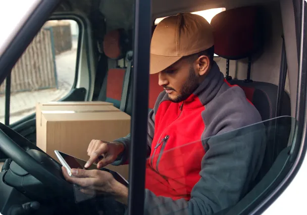 Een koerier achter het stuur van zijn bestelwagen, met zijn telefoon in de hand