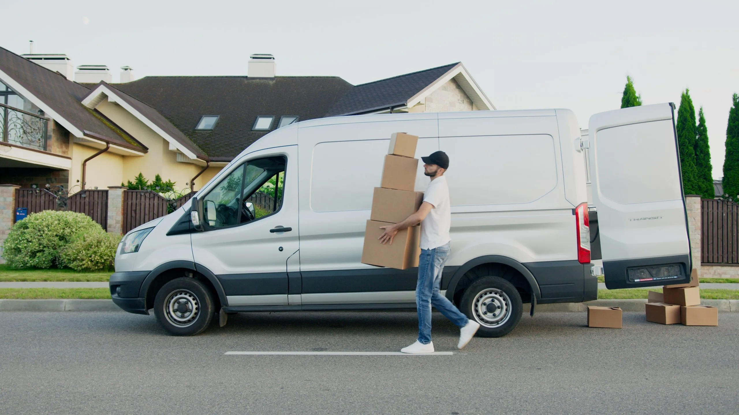 Livreur en camionnette qui porte des caisses en carton dans une rue résidentielle.