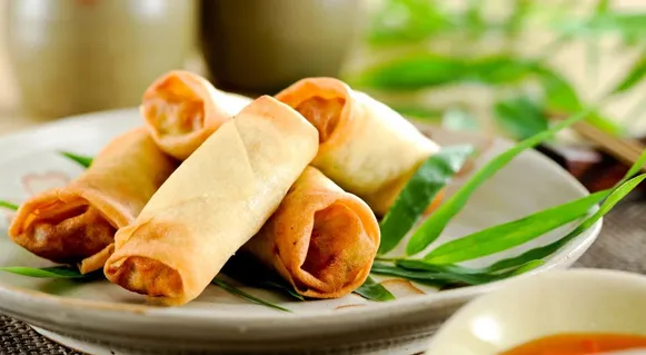 Des rouleaux de printemps dorés empilés sur une assiette, avec une coupelle de sauce