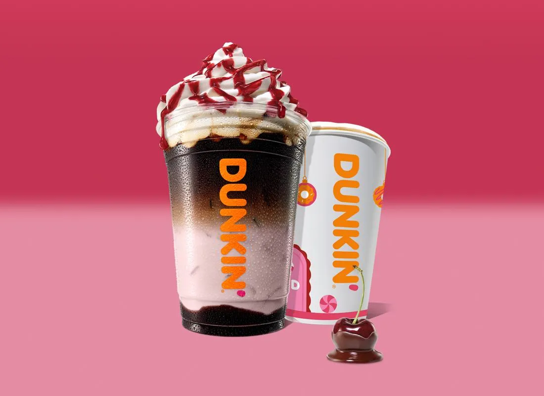 Een ijskoffie van Dunkin' met slagroom en kersensiroop, naast een warme Dunkin'-beker
